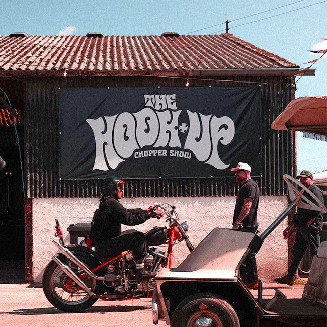 A shed with The Hook Up Chopper Show on a banner on the side, a man on a motorbike and a man standing next to him with a golf buggy in front of both