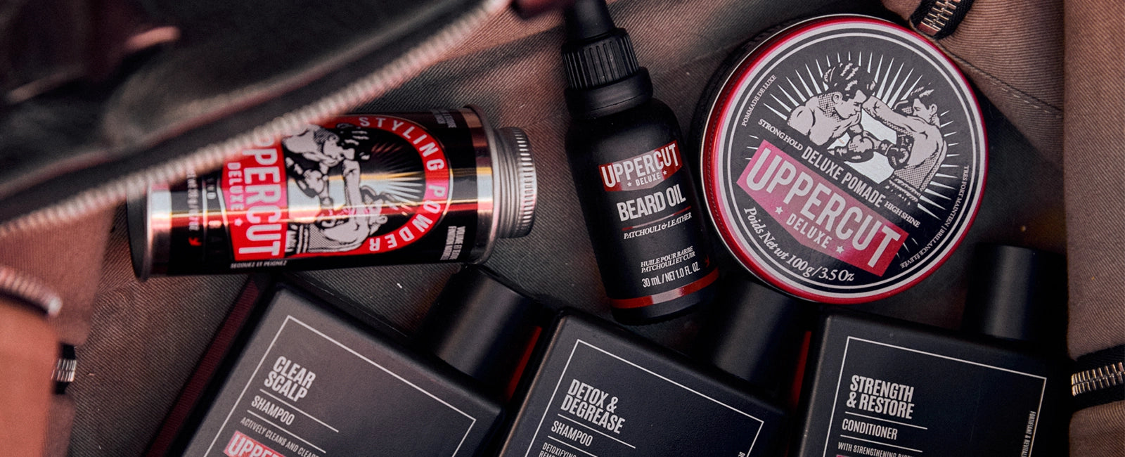 Uppercut Deluxe grooming products including a bottle, jar, and boxes on a textured surface.