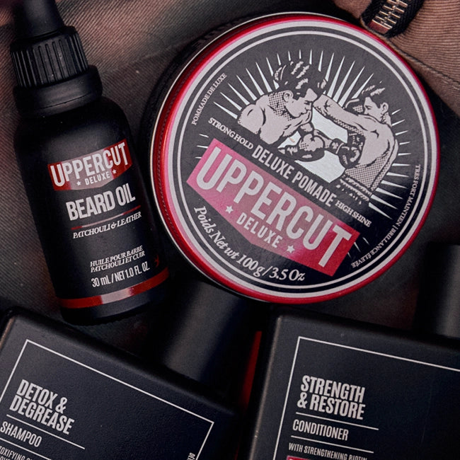 Uppercut Deluxe beard oil and pomade with product packaging on a wooden surface