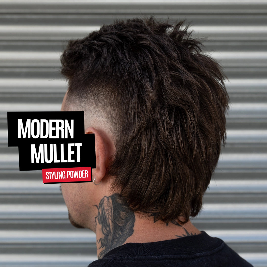 A man shown from the back wearing a dark brown textured modern mullet hairstyle with a faded undercut. The background is a corrugated metal wall.
