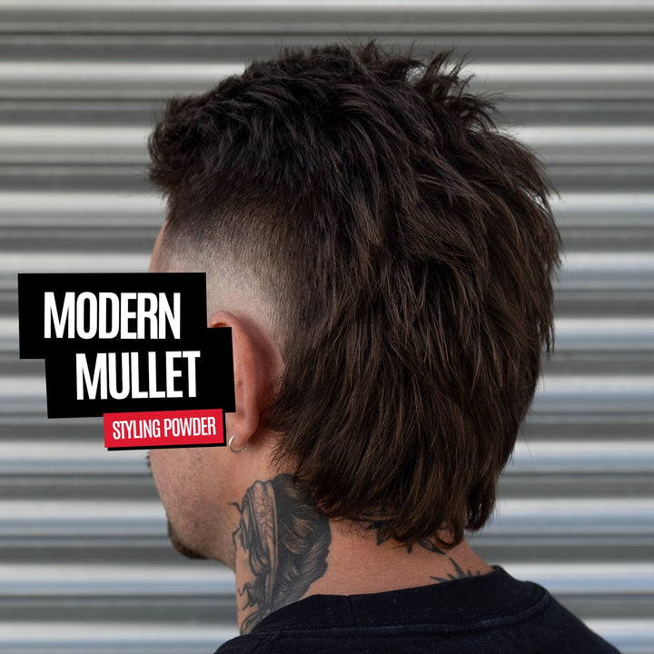 A man shown from the back wearing a dark brown textured modern mullet hairstyle with a faded undercut. The background is a corrugated metal wall.